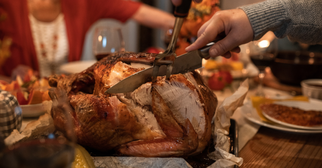 Image of turkey being carved on a table with people sitting around the table.