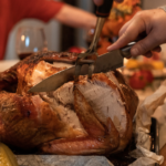 Image of turkey being carved on a table with people sitting around the table.